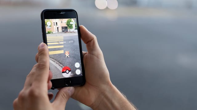 Jemand hält ein Smartphone, auf dem «Pokémon Go» gespielt wird in die Kamera. Jemand hält ein Smartphone, auf dem «Pokémon Go» gespielt wird in die Kamera.