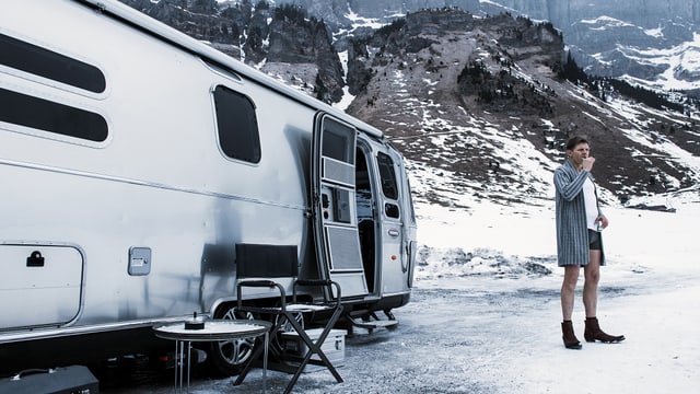Ein Mann steht neben einem Wohnwagen in einer verschneiten Landschaft. Er putzt sich die Zähne, trägt nur einen Bademantel, darunter Boxershorts. Ein Mann steht neben einem Wohnwagen in einer verschneiten Landschaft. Er putzt sich die Zähne, trägt nur einen Bademantel, darunter Boxershorts.