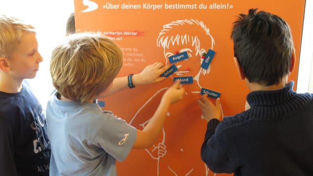 Drei Knaben vor einer Säule heften Worte an einen Körper. Drei Knaben vor einer Säule heften Worte an einen Körper.