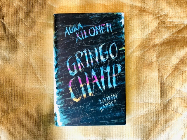 Der Roman «Gringo Champ» von Aura Xilonen vor goldigem Hintergrund Der Roman «Gringo Champ» von Aura Xilonen vor goldigem Hintergrund
