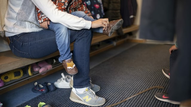 Eine Mutter zieht ihrem Kind in einer Kindertagesstätte die Schuhe an Eine Mutter zieht ihrem Kind in einer Kindertagesstätte die Schuhe an