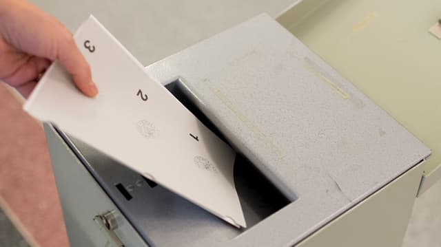 Eine Person wirft Unterlagen in einer Wahlurne