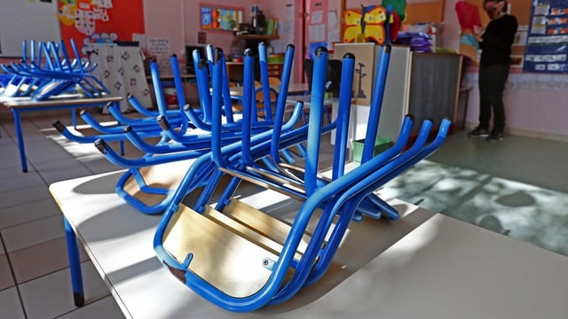 Blaue, aufeinander-gestapelte Stühle auf einem Tisch in einem Schulzimmer. 