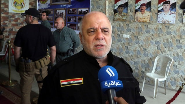 Al-Abadi en ina chasa, discurrind en il microfon. Al-Abadi en ina chasa, discurrind en il microfon.