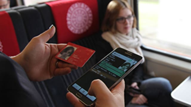Eine Zugbegleiterun hält in einer Hand einen SwissPass und in der anderen Hand ein Smartphone. Eine Zugbegleiterun hält in einer Hand einen SwissPass und in der anderen Hand ein Smartphone.