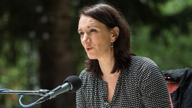 Ein Frau sitzt draussen an einem Tisch vor einem Mikrofon. Ein Frau sitzt draussen an einem Tisch vor einem Mikrofon.