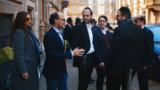 Ein Mann und eine Frau sprechen mit einer Gruppe jüdischer Männer mit Kippa. Ein Mann und eine Frau sprechen mit einer Gruppe jüdischer Männer mit Kippa.