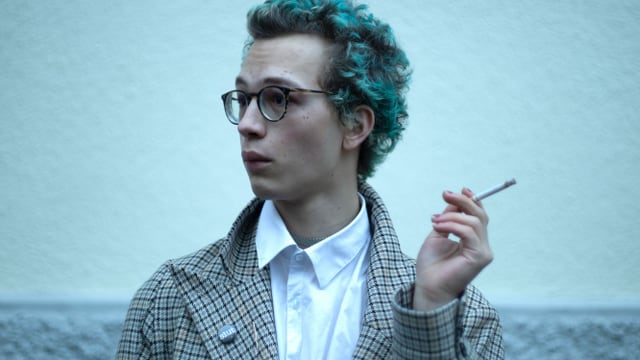 Junger Mann mit Brille und grünen Haaren raucht Zigarette Junger Mann mit Brille und grünen Haaren raucht Zigarette
