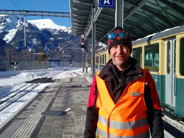 Mann in oranger Weste auf Bahnperron