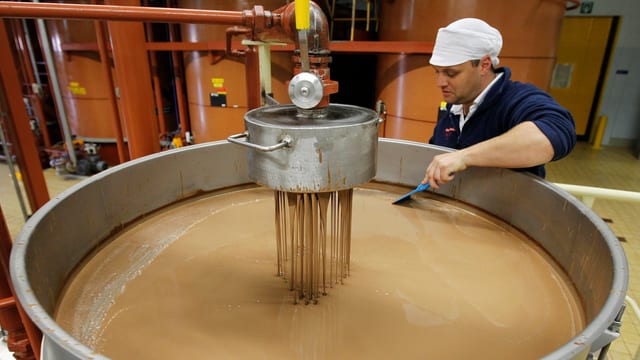 Ein Mitarbeiter von Barry Callebaut prüft flüssige Schokolade in einem grossen Kessel Ein Mitarbeiter von Barry Callebaut prüft flüssige Schokolade in einem grossen Kessel