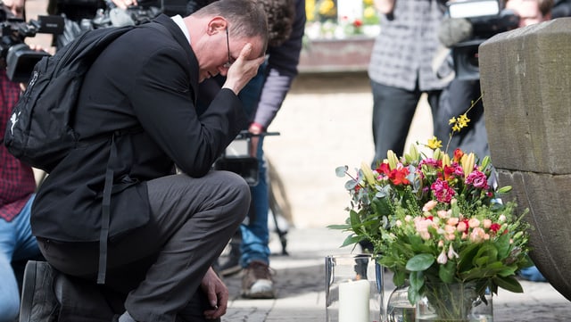 Ein Mann trauert, beobachten von zahlreichen Kameramännern, am Tatort. Ein Mann trauert, beobachten von zahlreichen Kameramännern, am Tatort.
