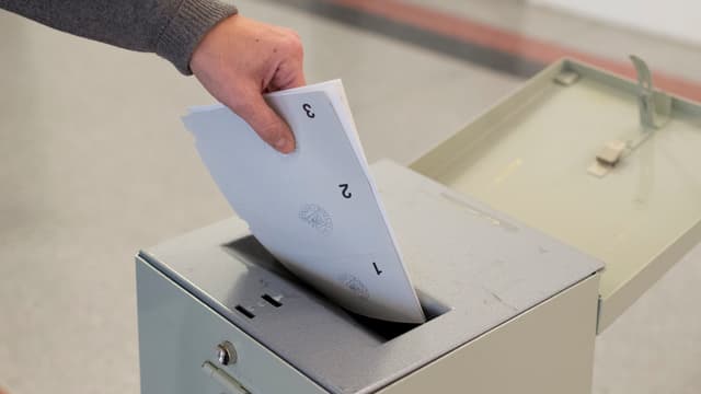 Jemand wirft einen Abstimmungszettel in eine Urne. Jemand wirft einen Abstimmungszettel in eine Urne.