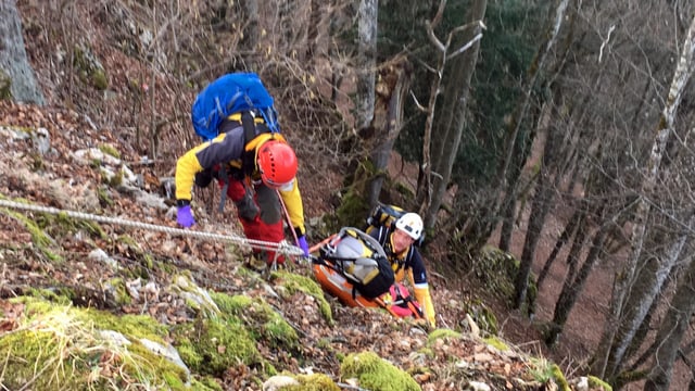 Zwei Retter mit Helmen halten eine Art Rettungsschlitten mit dem Patienten Zwei Retter mit Helmen halten eine Art Rettungsschlitten mit dem Patienten
