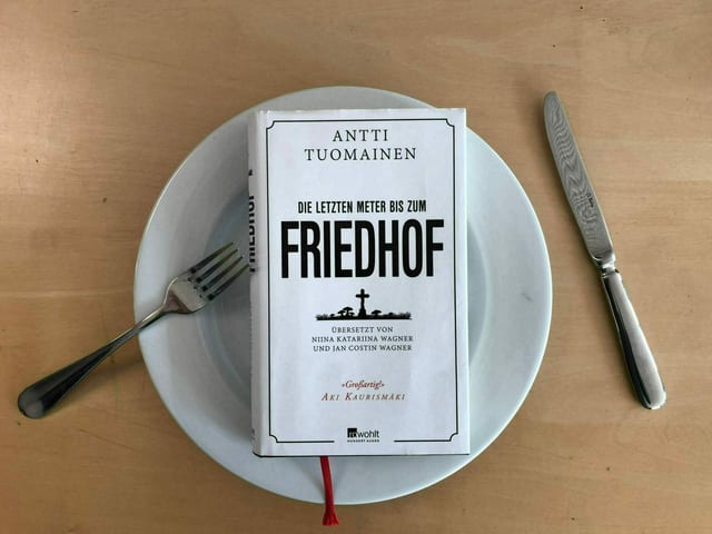 Das Buch «Die letzten Meter bis zum Friedhof» von Antti Tuomainen liegt auf einem weissen Teller. Messer und Gabel liegen hingeworfen daneben. Das Buch «Die letzten Meter bis zum Friedhof» von Antti Tuomainen liegt auf einem weissen Teller. Messer und Gabel liegen hingeworfen daneben.