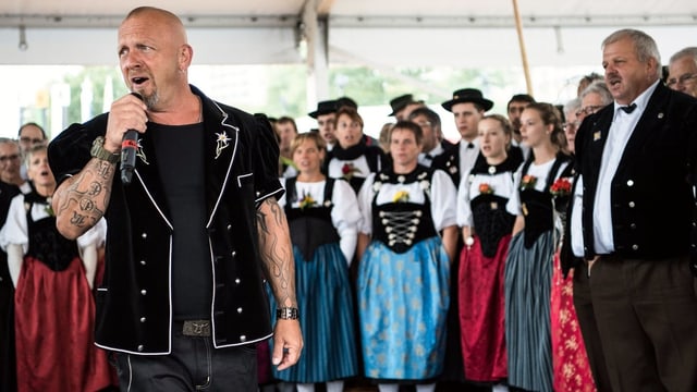 Der Sänger Gölä mit Mikrophon und Jodelchor im Hintergrund. Der Sänger Gölä mit Mikrophon und Jodelchor im Hintergrund.