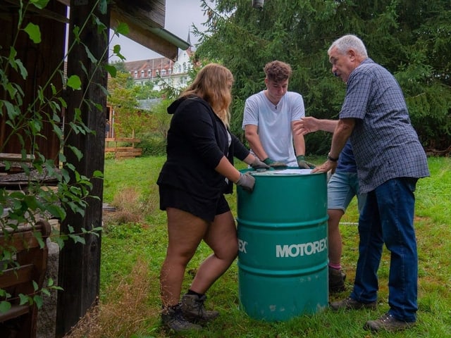Drei Menschen stehen um eine Tonne Drei Menschen stehen um eine Tonne