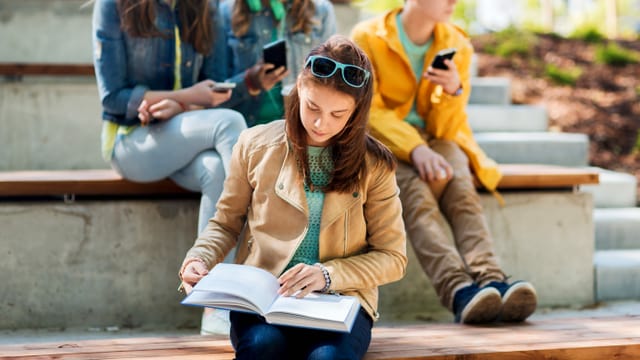 Mädchen liest ein Buch abseits einer Gruppe von Jugendlichen Mädchen liest ein Buch abseits einer Gruppe von Jugendlichen
