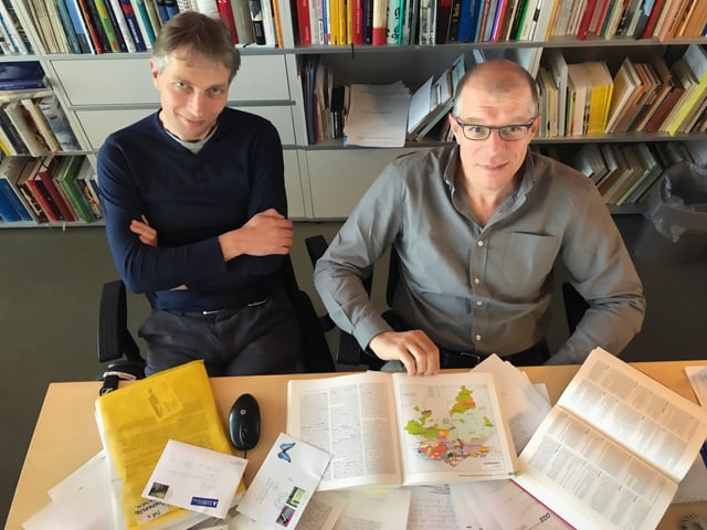 Zwei Herren sitzen vor einer Bücherwand, davor viele Briefe von Hörerinnen und Hörern. Zwei Herren sitzen vor einer Bücherwand, davor viele Briefe von Hörerinnen und Hörern.