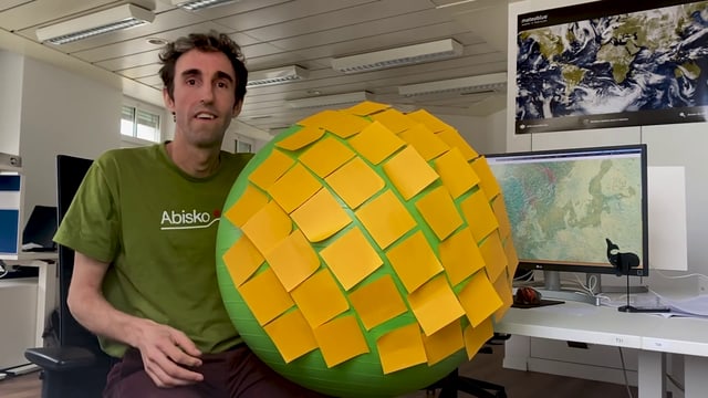 Ein Mann sitzt mit einem mit Post-It-Klebern vollgeklebten grossen grünen Gummiball vor dem Computer Ein Mann sitzt mit einem mit Post-It-Klebern vollgeklebten grossen grünen Gummiball vor dem Computer