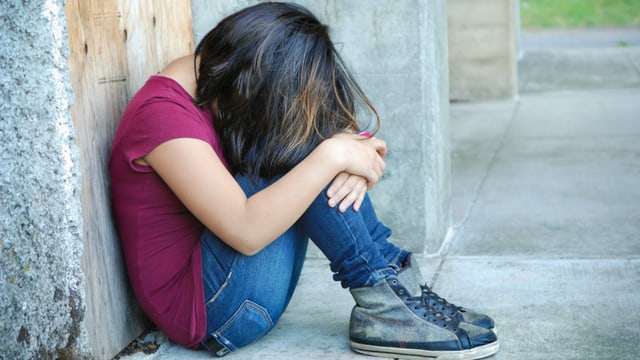 Kind mit mittellangem Haar sitzt vornübergebeugt auf dem Boden. Kind mit mittellangem Haar sitzt vornübergebeugt auf dem Boden.
