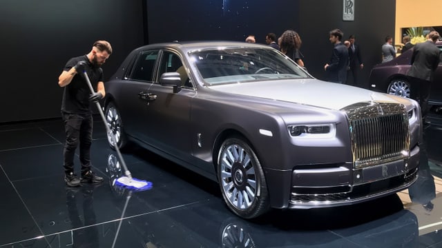 Ein Mann putzt neben einem Luxusauto den Boden. Ein Mann putzt neben einem Luxusauto den Boden.
