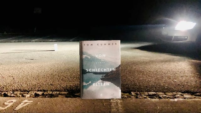 Der Roman «Von schlechten Eltern» von Tom Kummer steht auf dem Asphalt. Hinten leuchteten die Scheinwerfer eines Autos in der Nacht. Der Roman «Von schlechten Eltern» von Tom Kummer steht auf dem Asphalt. Hinten leuchteten die Scheinwerfer eines Autos in der Nacht.