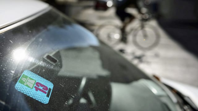 Eine Vignette klebt an einer Autoscheibe. Hinter dem parkierten Auto fährt ein Velofahrer vorbei. (Keystone) Eine Vignette klebt an einer Autoscheibe. Hinter dem parkierten Auto fährt ein Velofahrer vorbei. (Keystone)