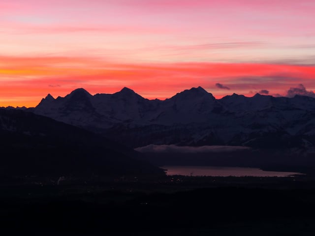 Eine dunkle Bergkette liegt unter einem orange bis violett gefärbten Himmel.