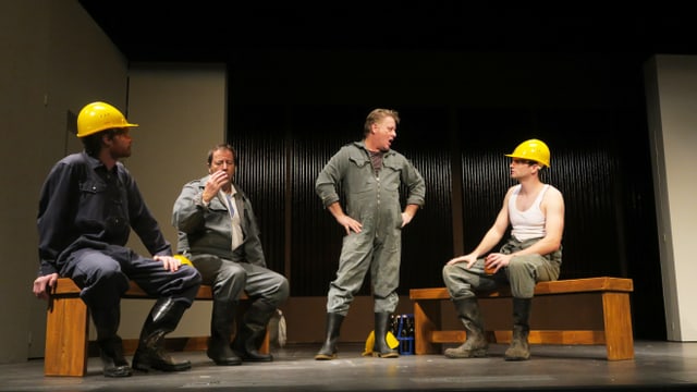 Szene in einem Landtheater: Arbeiter mit gelben Schutzhelmen stehen und sitzen auf der Bühne. Szene in einem Landtheater: Arbeiter mit gelben Schutzhelmen stehen und sitzen auf der Bühne.
