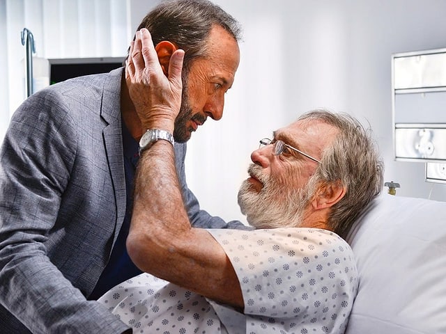 Ein Mann im Spitalbett umarmt einen Besucher. Ein Mann im Spitalbett umarmt einen Besucher.