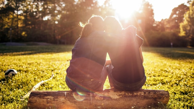 zwei Mädchen sitzen draussen auf einer Wiese und umarmen sich zwei Mädchen sitzen draussen auf einer Wiese und umarmen sich