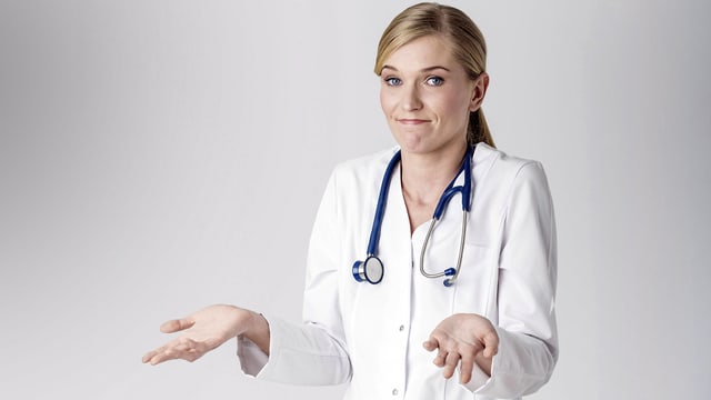Ärztin in weissem Kittel zuckt hilflos lächelnd mit den Schultern