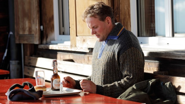 Ein Mann sitzt am draussen an einem Restauranttisch vor einer Flasche Bier. Ein Mann sitzt am draussen an einem Restauranttisch vor einer Flasche Bier.