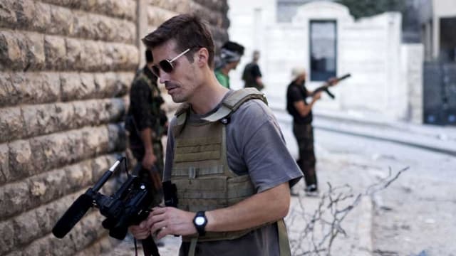 Kriegsreporter Foley mit einer TV-Kamera im Vordergrund – im Hintergrund ein Rebell mit einer Maschinenpistole. Kriegsreporter Foley mit einer TV-Kamera im Vordergrund – im Hintergrund ein Rebell mit einer Maschinenpistole.