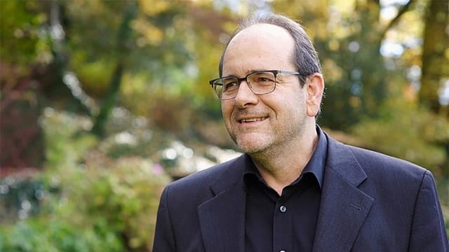 Ein Mann in Anzug und Brille, dahinter Wald. Ein Mann in Anzug und Brille, dahinter Wald.