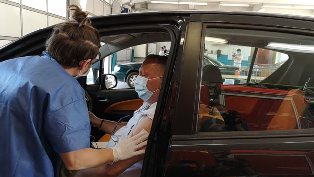 Frau wischt druch Auotüre mit Tüchlein Oberarm von Mann in Auto ab. Frau wischt druch Auotüre mit Tüchlein Oberarm von Mann in Auto ab.