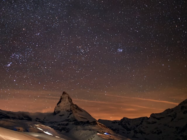Nacht mit Sternenhimmel. Unten ein pyramidenförmiger Berg, das Matterhorn.
