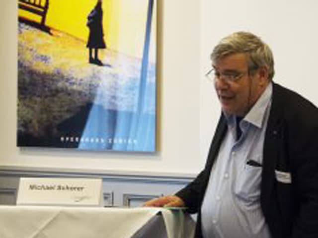Mit grauen Haar und Brille auf einem Podium, Publikumsfragen beantwortend. Mit grauen Haar und Brille auf einem Podium, Publikumsfragen beantwortend.