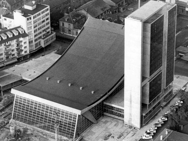 Das Kongresshaus Biel: Es besteht aus zwei Gebäudeteilen. Der erste ist ein Hochhaus mit einer Glasfront und das andere ist ein flacheres Gebäude mit nach innen geschwungener Decke. Die Fassade zur Strasse hin ist ebenfalls aus Glas. Das Kongresshaus Biel: Es besteht aus zwei Gebäudeteilen. Der erste ist ein Hochhaus mit einer Glasfront und das andere ist ein flacheres Gebäude mit nach innen geschwungener Decke. Die Fassade zur Strasse hin ist ebenfalls aus Glas.