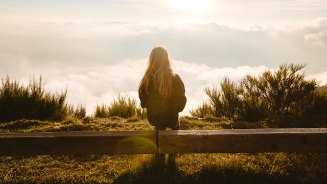 Eine junge Frau sitzt auf einer Bank. Vor ihr ist ein Wolkenmeer zu sehen. Eine junge Frau sitzt auf einer Bank. Vor ihr ist ein Wolkenmeer zu sehen.