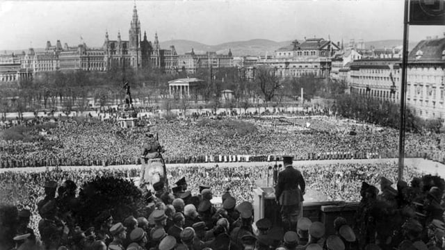 Schwarz-weiss Aufnahme mit Hitler von hinten im Vordergrund und einer Menschenmasse im Hintergrund. Schwarz-weiss Aufnahme mit Hitler von hinten im Vordergrund und einer Menschenmasse im Hintergrund.