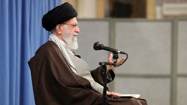 Chamenei mit schwarzem Turban sitzt vor einem Mikrofon. Chamenei mit schwarzem Turban sitzt vor einem Mikrofon.