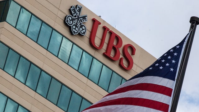 Logo der UBS an einem Gebäude – davor ist ein Ausschnitt der US-Fahne zu sehen Logo der UBS an einem Gebäude – davor ist ein Ausschnitt der US-Fahne zu sehen