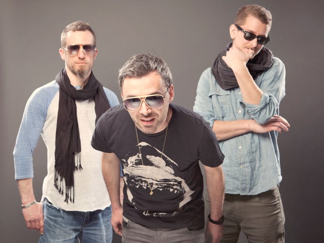 Drei Männer, alle mit Sonnenbrille, stehen vor grauem Hintergrund. Drei Männer, alle mit Sonnenbrille, stehen vor grauem Hintergrund.