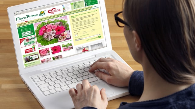 Symbolbild: Eine Frau sitzt an einem Laptop, darauf eine Internet-Seite geöffnet, auf der man Blumensträusse bestellen kann.