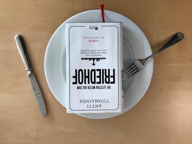 Das Buch «Die letzten Meter bis zum Friedhof» von Antti Tuomainen liegt auf einem weissen Teller. Messer und Gabel liegen hingeworfen daneben. Das Buch «Die letzten Meter bis zum Friedhof» von Antti Tuomainen liegt auf einem weissen Teller. Messer und Gabel liegen hingeworfen daneben.