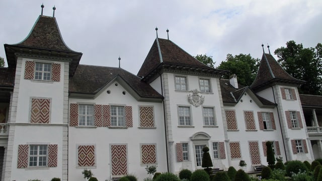 Bild des Schlosses von aussen. Es besteht aus mehreren Gebäudeteilen. Die Fensterläden sind rot-weiss angestrichen.