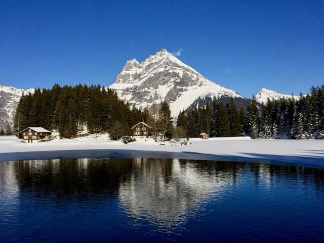 Ein blauer Alpsee liegt in einer herrlich verschneiten Berglandschaft. Der Himmel ist praktisch wolkenlos.