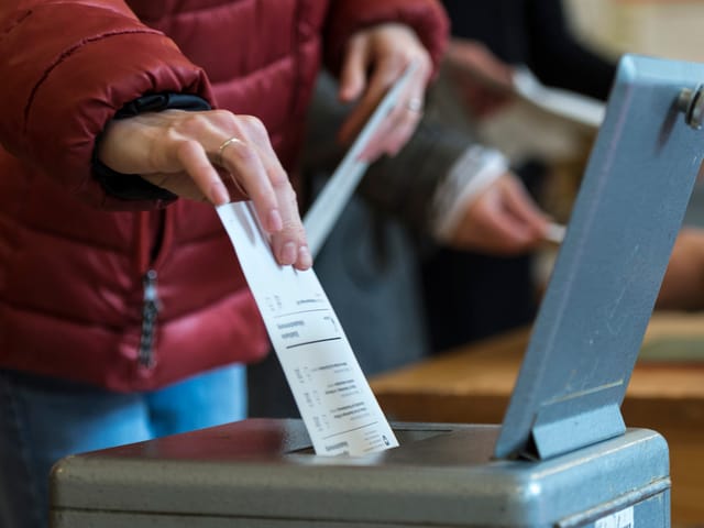 Hand wirft Stimmzettel in eine Urne.