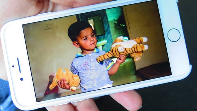 Auf einem Bildschirm ist ein Foto von einem Jungen, der zwei Kuscheltiere trägt. Auf einem Bildschirm ist ein Foto von einem Jungen, der zwei Kuscheltiere trägt.